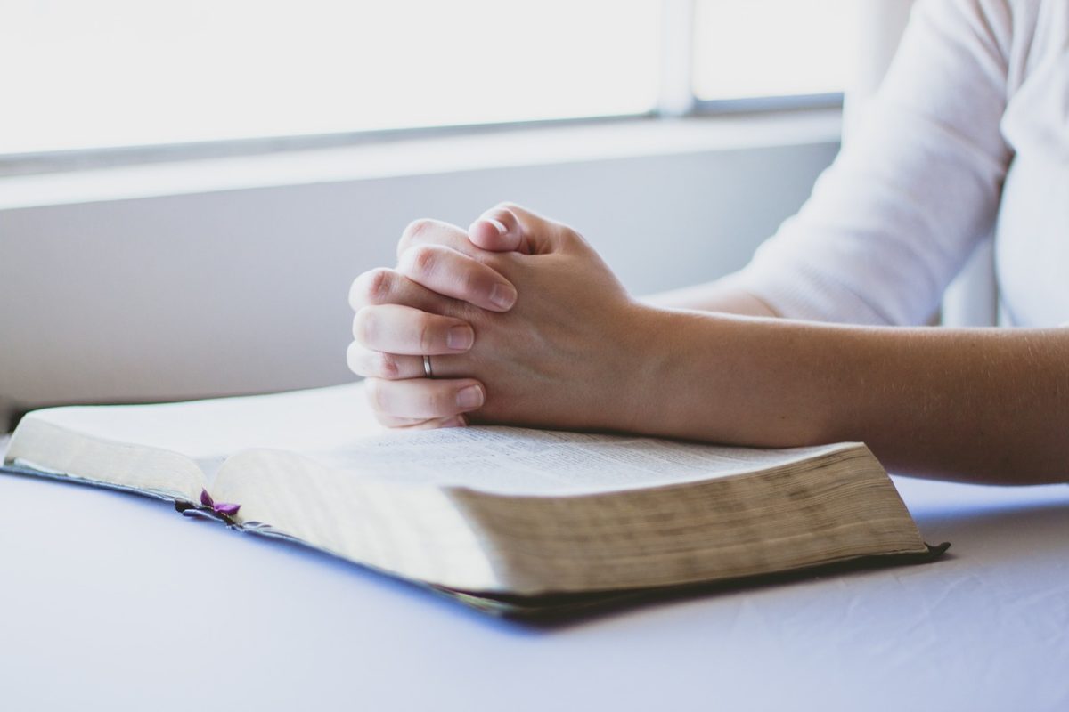 Praying woman with hands on bible.